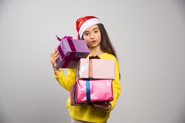 Kid dressed in Santa Claus red hat carrying a lot of Christmas presents. High quality photo