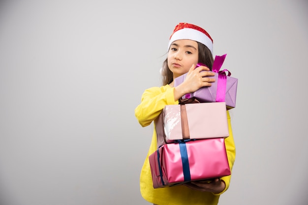 Kid dressed in Santa Claus red hat carrying a lot of Christmas presents. High quality photo