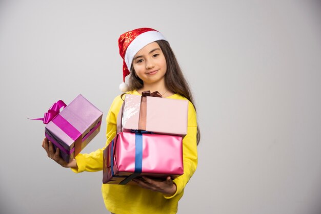 Kid dressed in Santa Claus red hat carrying a lot of Christmas presents. High quality photo