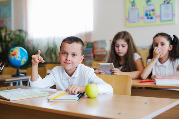 Free photo kid gesturing at table in classroom