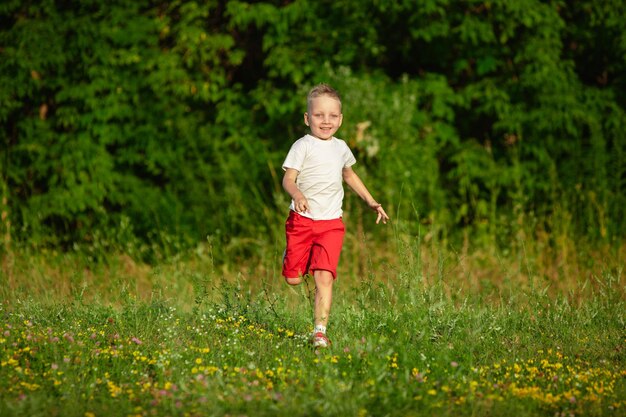 子供、夏の日差しの中で牧草地を走っている小さな男の子