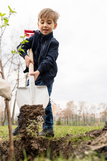 Foto gratuita kid cercando di piantare un albero all'aperto