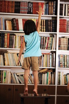 Малыш пытается найти книгу в библиотеке Premium Фотографии