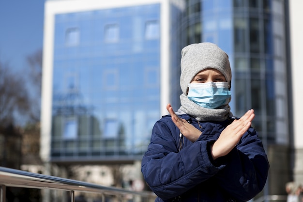 Kid with medical mask showing x sign outside