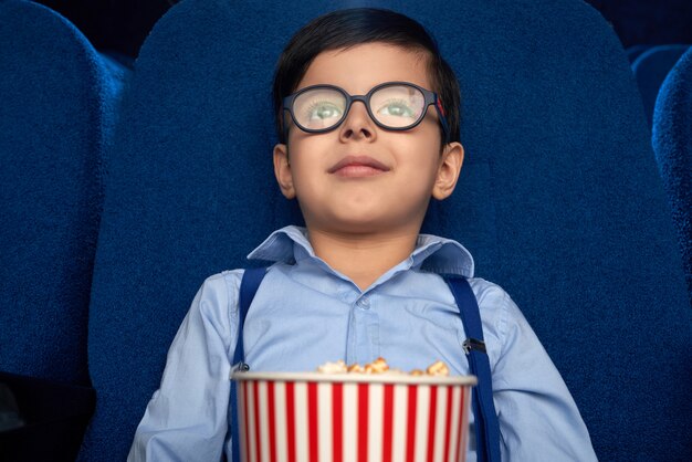 Kid with popcorn bucket watching cartoon in cinema.