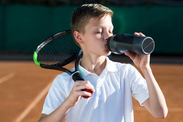 Kid with racket on the shoulder and drinking water