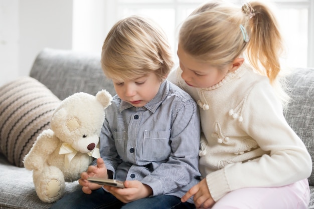 KIds boy and girl using smartphone together sitting on sofa