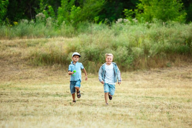 Дети, дети бегают по лугу в лучах летнего солнца. Выгляди счастливым, жизнерадостным, с искренними яркими эмоциями. Симпатичные кавказские мальчики и девочки.