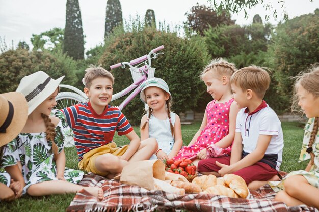 Kids fashion concept. group of teen boys and girls sitting at green grass at park. Children colorful clothes, lifestyle, trendy colors concepts.