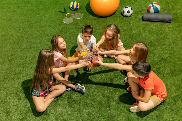 Foto gratuita concetto di moda per bambini. il gruppo di ragazzi e ragazze adolescenti seduti sull'erba verde al parco. bambini vestiti colorati, stile di vita, concetti di colori alla moda.