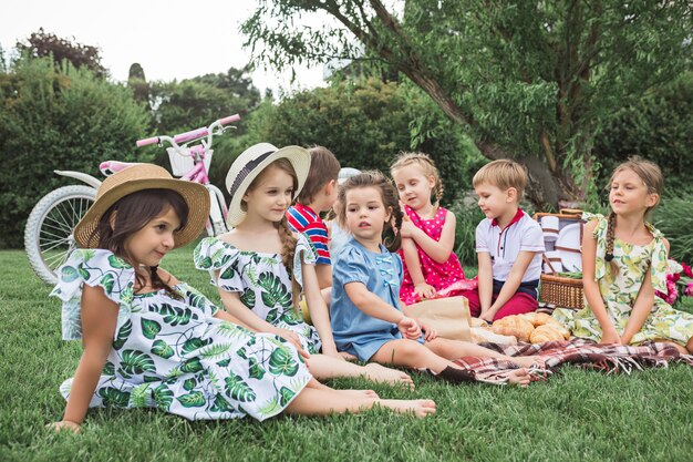 Kids fashion concept. The group of teen boys and girls sitting at green grass at park.