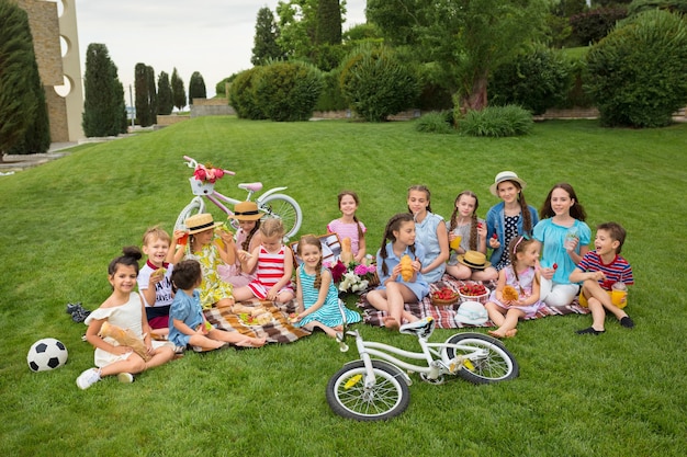 키즈 패션 개념. 공원에서 푸른 잔디에 앉아 십 대 소녀의 그룹. 어린이 화려한 옷, 라이프 스타일, 유행 색상 개념.