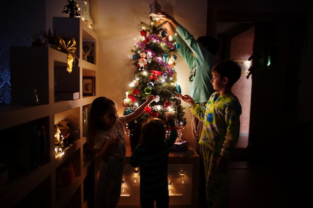 저녁 집에 빛나는 화환으로 크리스마스 트리를 보고 있는 아이들.