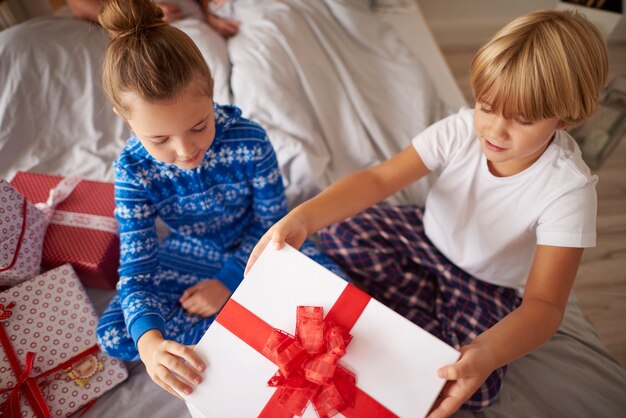 Kids opening big Christmas gift in the bed