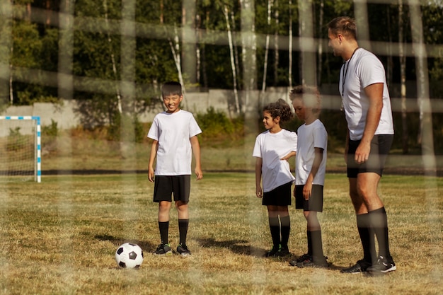 Foto gratuita bambini che giocano a calcio sotto la supervisione di un allenatore di calcio