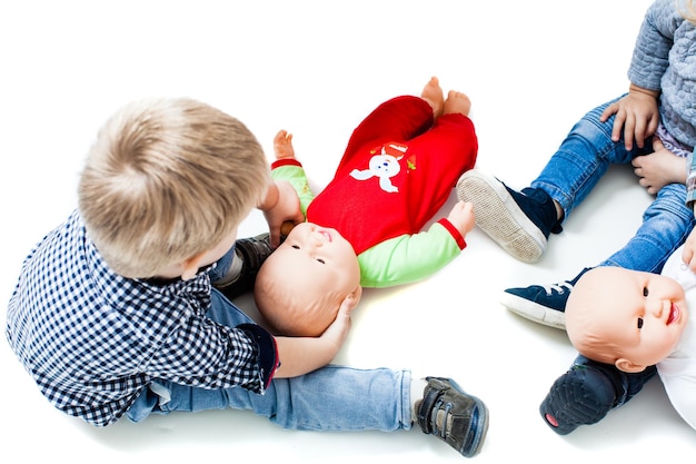 Дети играют в куклы. мальчик и девочки сидят на полу в детском саду и играют семьей. понятие отцовства
