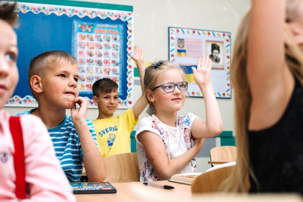 Бесплатное фото Дети, сидящие на школьных столах, поднимая руки