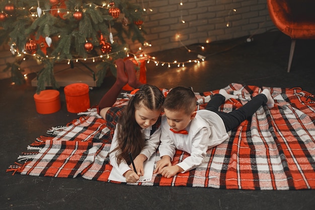 Kids sitting near Christmas tree. Children write a letter to Santa Claus.