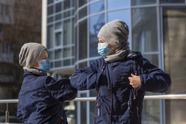 Kids touching elbows while wearing medical masks outside