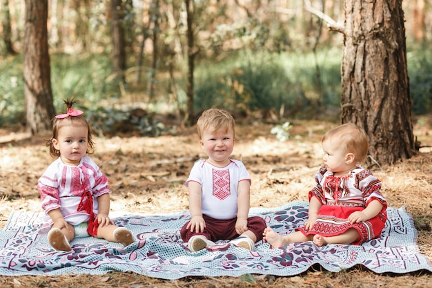 Kids in traditional ukrainian clothes play in forest in sunbeam. boy and two girls