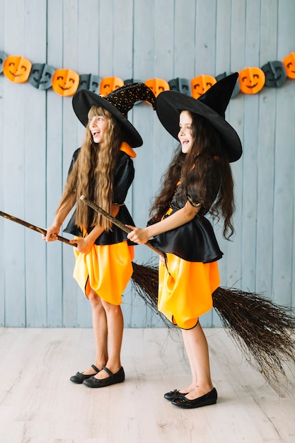 Kids in witch costumes holding broomsticks between legs