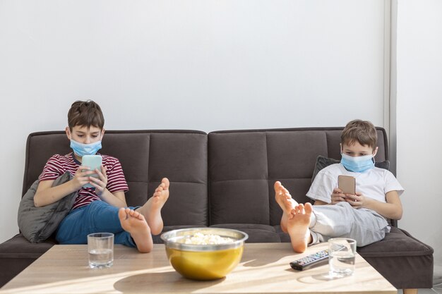 自宅でスマートフォンで遊ぶ医療用マスクを持つ子供