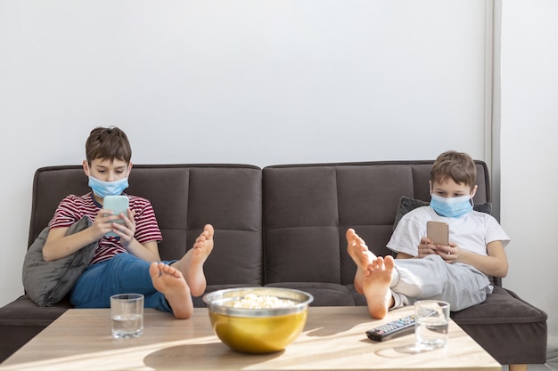 Дети с медицинскими масками играют на смартфонах дома