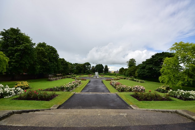 Kilkenny castle garden surrounded by greenery under a cloudy sky in Ireland