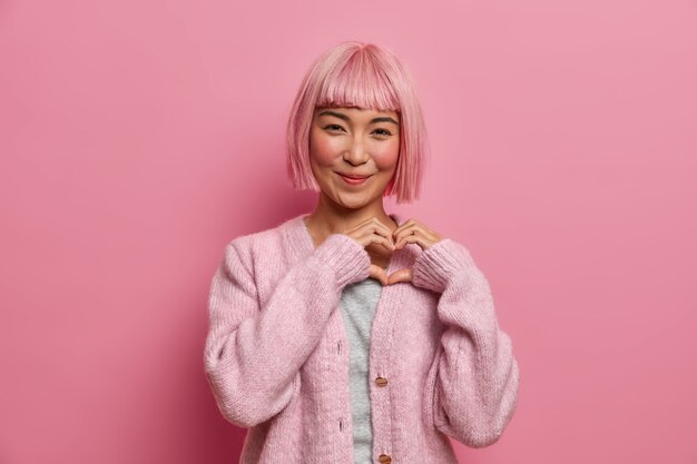 Kind positive amiable Asian woman with bob hairstyle, makes heart shape gesture