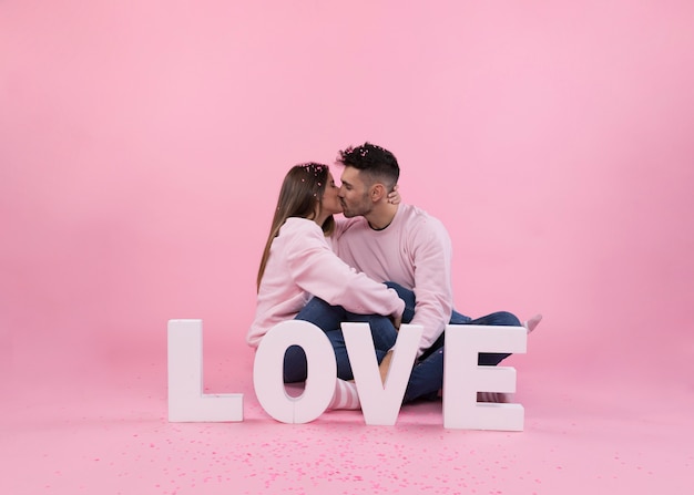 Kiss of young couple near big love sign and confetti