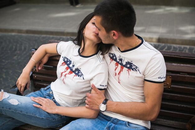 Kissing couple in similar t-shirts on bench