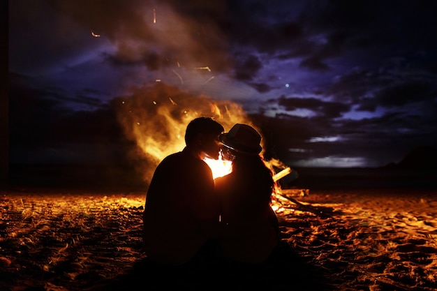 Kissing couple sitting by a beach bonfire