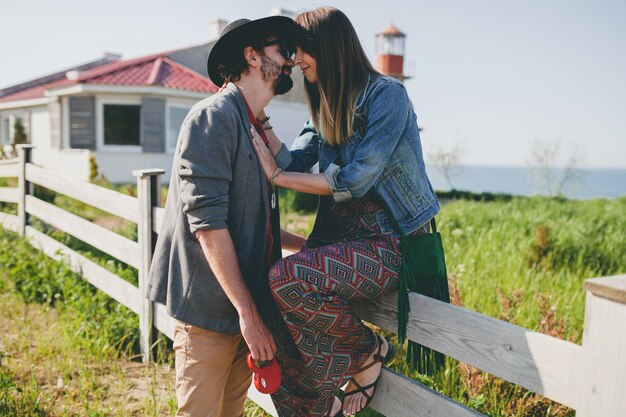 Kissing happy young stylish hipster couple in love walking in countryside, summer style boho fashion