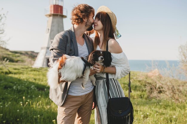 Kissing stylish hipster couple in love walking with dog in countryside, summer style boho fashion, romantic