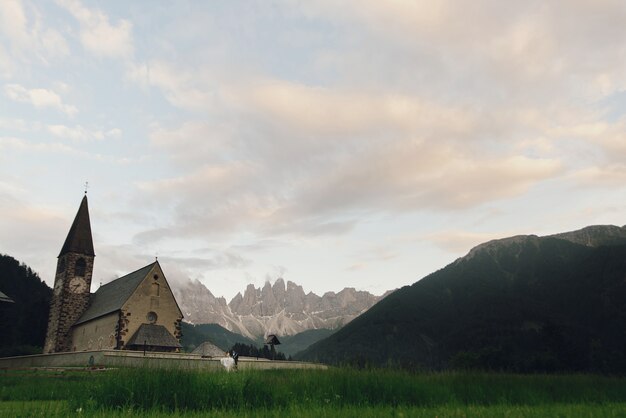 Kissing wedding couple stands before stone church in mountains 