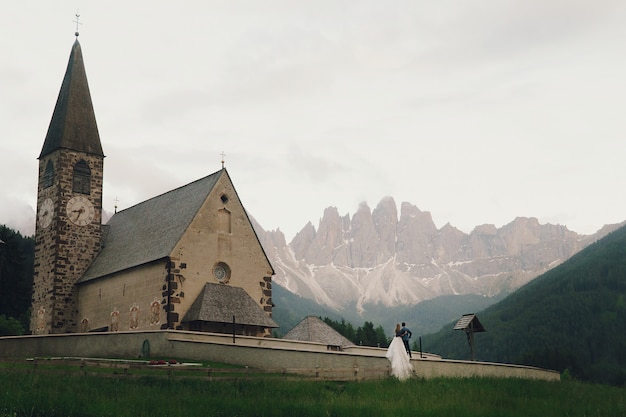 Free photo kissing wedding couple stands before stone church in mountains