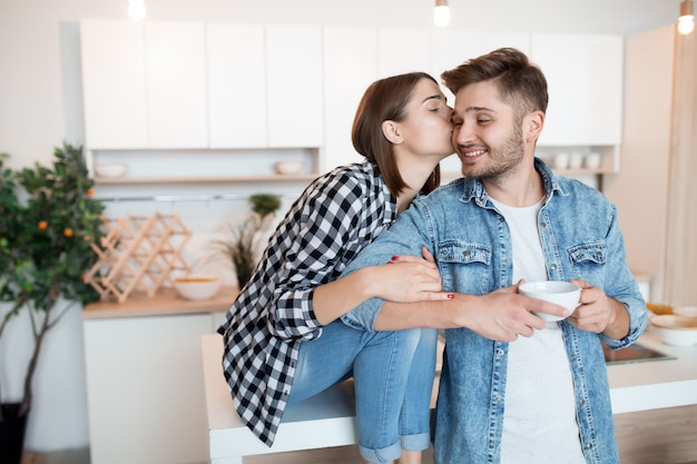 Baciare giovane uomo felice e donna in cucina, colazione, coppia insieme al mattino, sorridente, tè