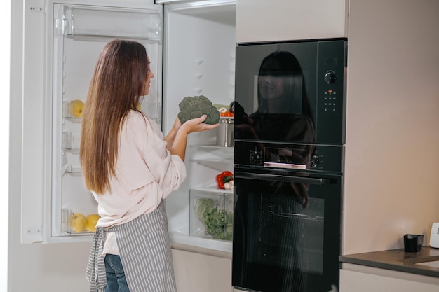 Free photo in the kitchen. young housewife standing near the fridge in the kitchen