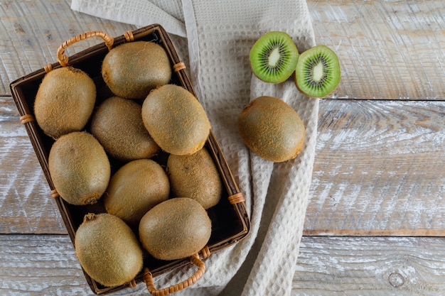 Киви в корзине на деревянном и кухонном полотенце. плоская планировка