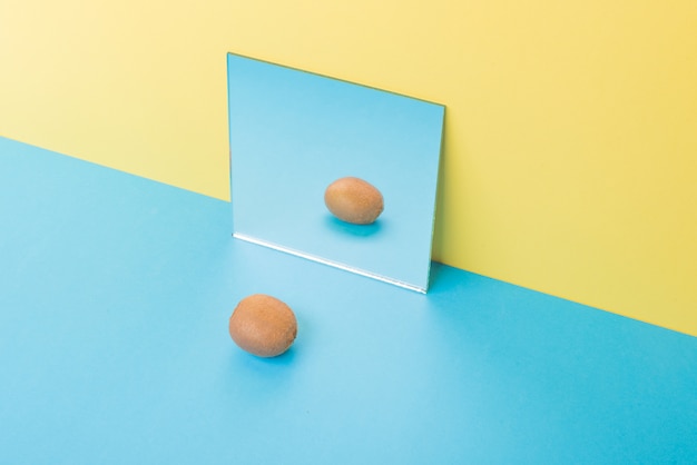 Kiwi on blue table isolated on yellow near mirror