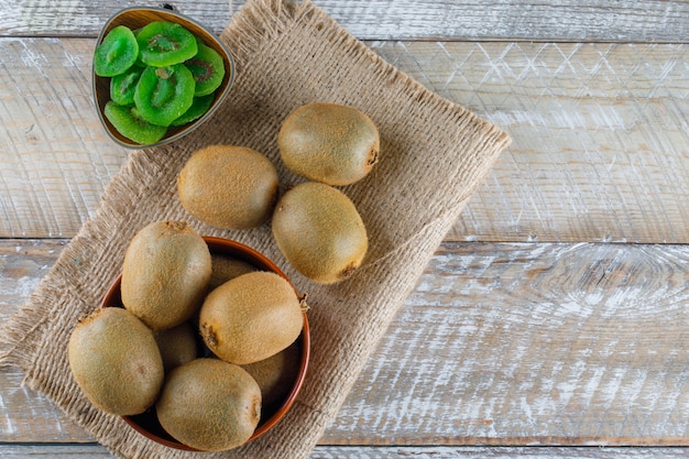 Kiwi in a bowl with dried slices flat lay on wooden and piece of sack