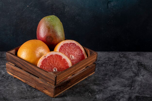 Kiwi, orange and grapefruit slices in a wooden tray on a dark marble