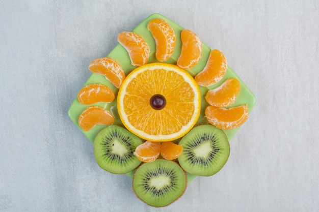 Free photo kiwi, orange and tangerine slices on green plate. high quality photo