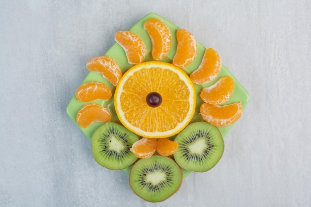 Kiwi, orange and tangerine slices on green plate. High quality photo