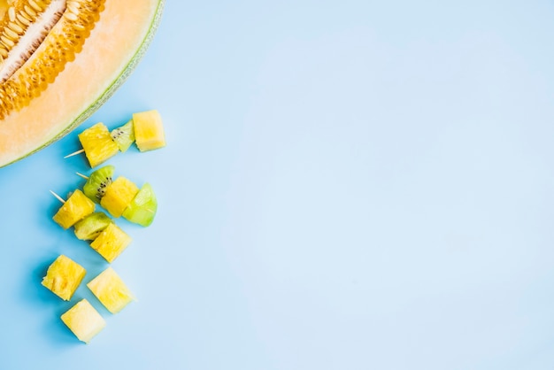 Kiwi and pineapple canape near halved melon on blue backdrop