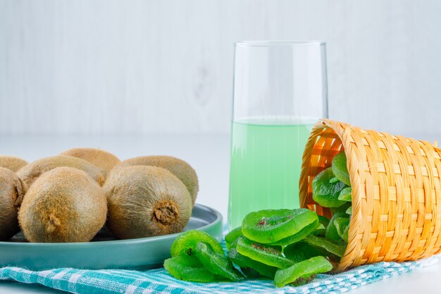 Kiwi in a plate with dried kiwi, drink side view on white and picnic cloth background