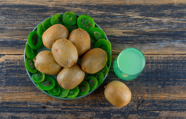 Kiwi with dried slices, drink in a tray on wooden background, flat lay.