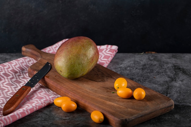 A kiwi on a wooden cutting board with some kinkans and a knife