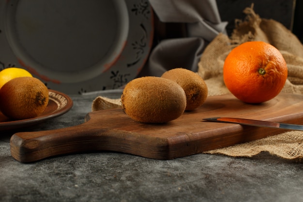 Kiwies and orange on a wooden board.