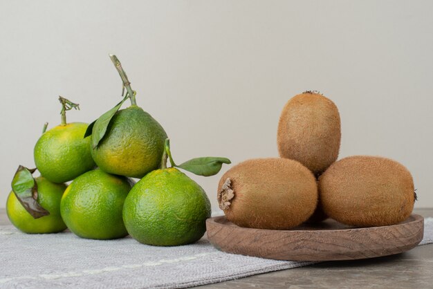 Kiwis and fresh tangerines on gray tablecloth.